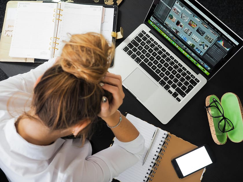 Top-down view of a person with a bun at a desk, working on a silver laptop surrounded by notebooks and a planner.